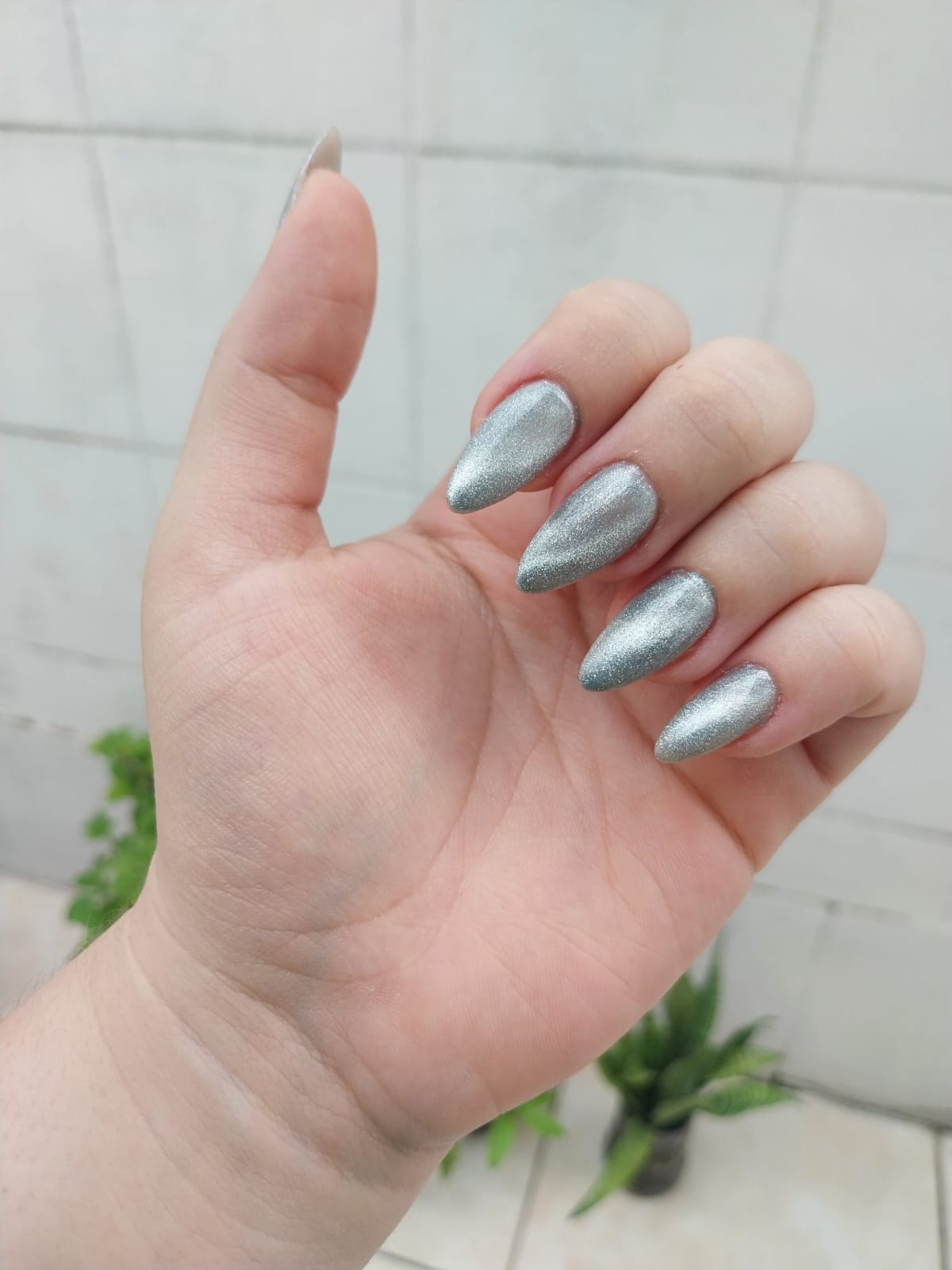 Unhas longas formato stiletto com esmaltação metálica prata efeito cat eye