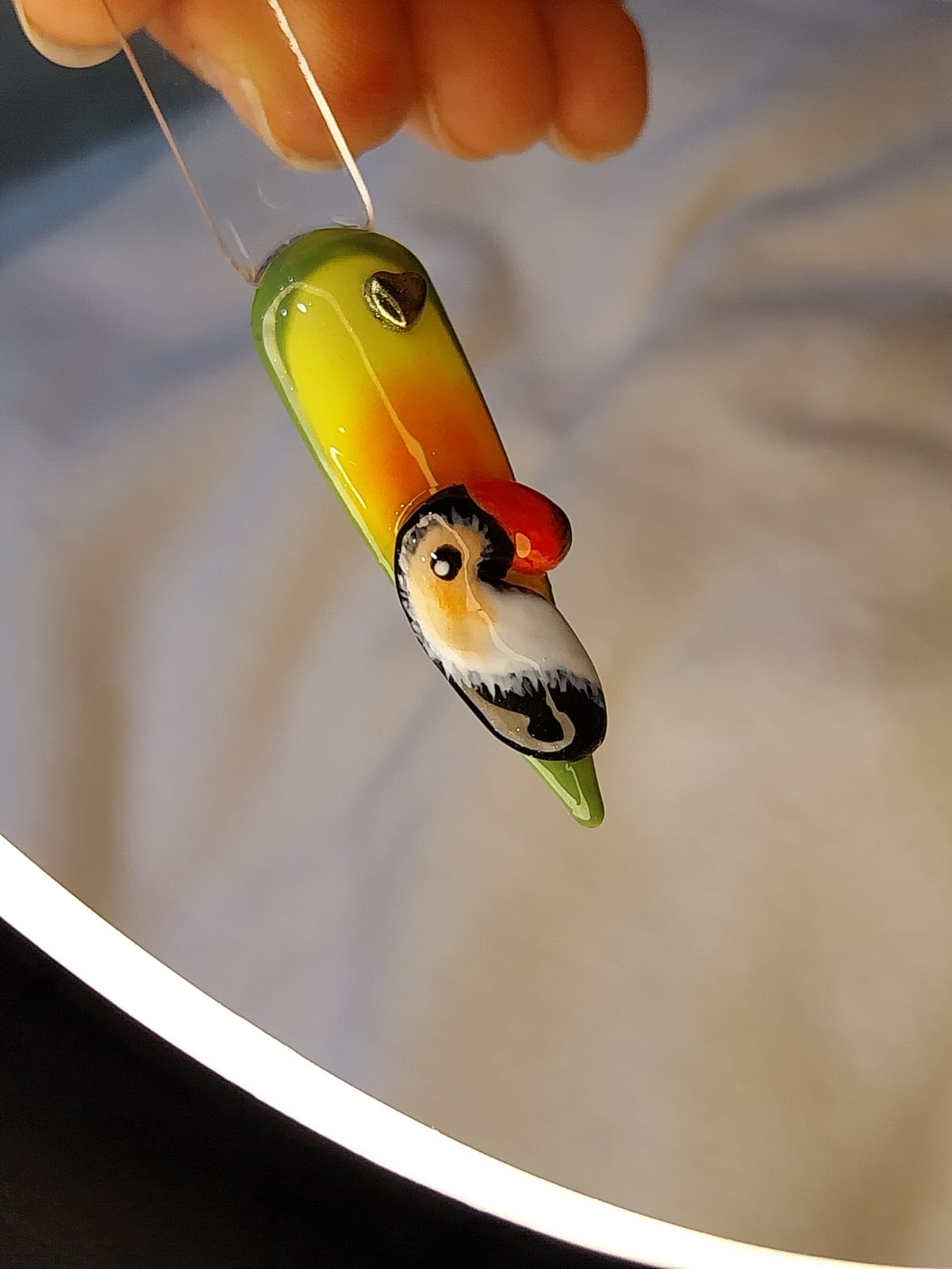 Nail art autoral em 3D de uma ave colorida sobre unha em degradê verde e amarelo